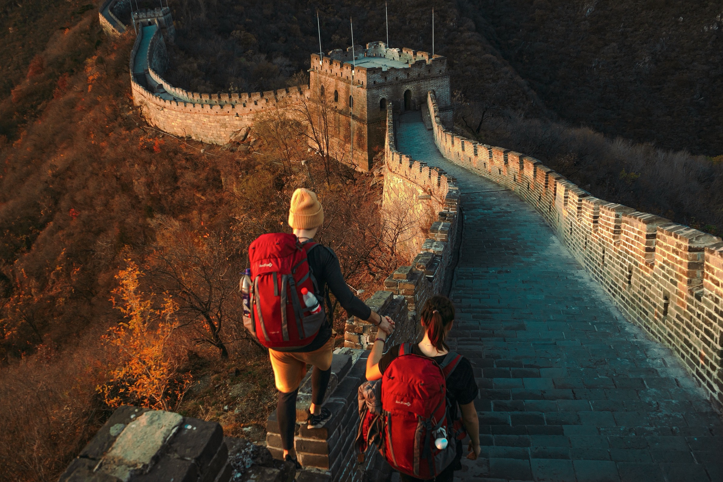 Two travellers with backpacks walking an empty stretch of the Great Wall at sunset