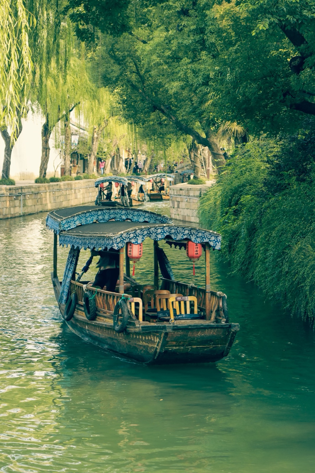 A wooden canal boat with red lanterns moored under willow trees in a water town